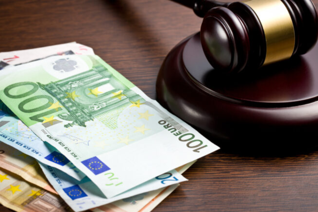 Drewniany młotek sędziowski leżący na stosie banknotów o nominałach 100 i 200 euro, symbolizujący wysokie kary finansowe oraz konsekwencje prawne naruszenia przepisów.
